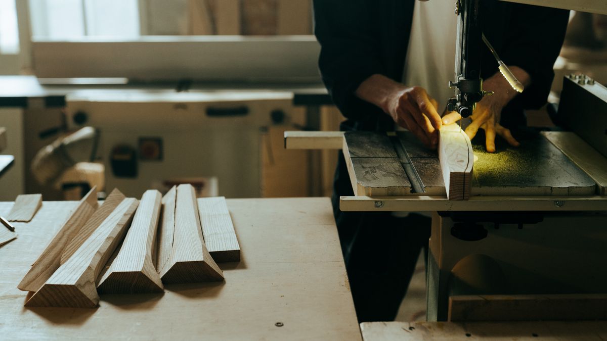 Artisan charpentier utilisant une scie à ruban pour façonner une pièce de bois dans un atelier équipé